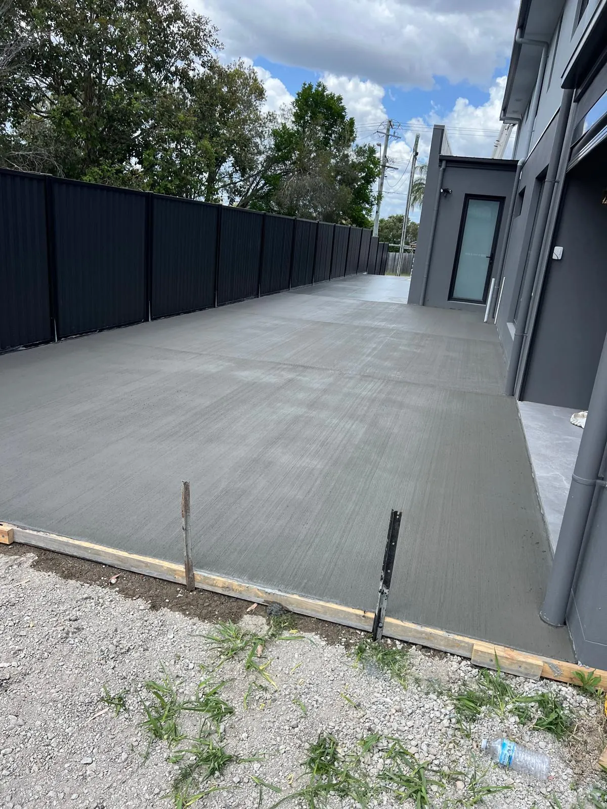 Freshly poured broom-finish concrete slab along side of a Brisbane home with Colorbond fence